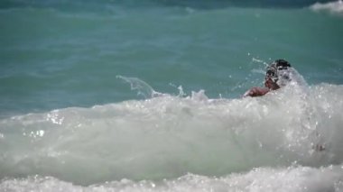 Gözlüklü küçük sağlıklı bir çocuk yaz tatilinde deniz dalgalarında zıplama oyunu oynuyor.