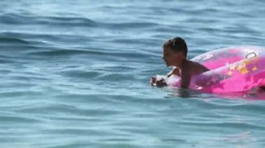 Tatil tatili sırasında, deniz kenarında, suyun içinde lastik hava çemberinde yüzen küçük bir çocuk.