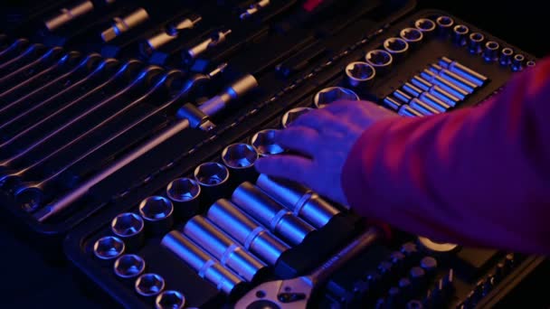 Workman in red clothes taking and connecting head socket and ratchet wrench tool from toolkit lit with yellow and blue light in darkness — Vídeos de Stock