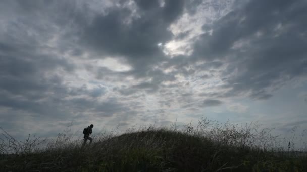 Sırt çantalı sağlıklı bir yetişkin adam alçak tepelerde yürüyor ve dışarıda yürüyüş yaparken yoğun bulut bulutlarının altında duruyor. — Stok video