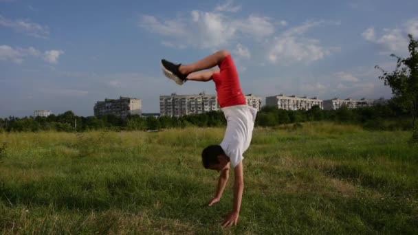 Actif sain petit caucasien enfant en short rouge et maillot blanc faisant ralentir le saut périlleux dans vert parc entendre les bâtiments de la ville urbaine — Video