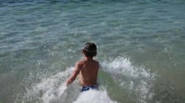 Yüzme şortu ve maske takmış, yaz tatili aktiviteleri sırasında deniz suyuna dalan sağlıklı küçük bir çocuğu eğlence amaçlı kovalamak.