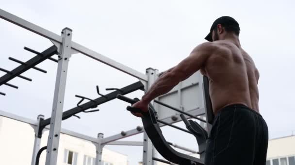 Hombre joven fuerte en la tapa que tira del peso pesado en la máquina de ejercicio durante el entrenamiento al aire libre del levantamiento de pesas — Vídeos de Stock