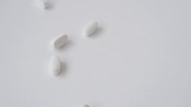 Birçok beyaz tıbbi vitamin hapının besin takviyesi hapları yavaş çekimde parlak yüzeye düşüyor.