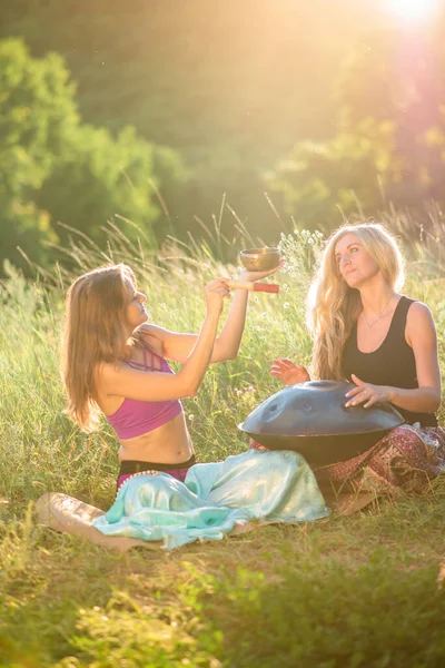 Young women play and sing on the musical instrument Handpan. Practice meditation at sunset