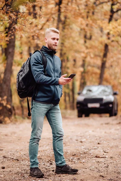 The man travels by car. The guy on the phone looks at where he is on the navigator. Hiker lost in the autumn forest concept.