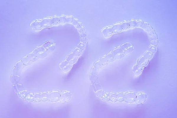 Invisible dental teeth brackets tooth aligners on purple background. Plastic braces dentistry retainers to straighten teeth.