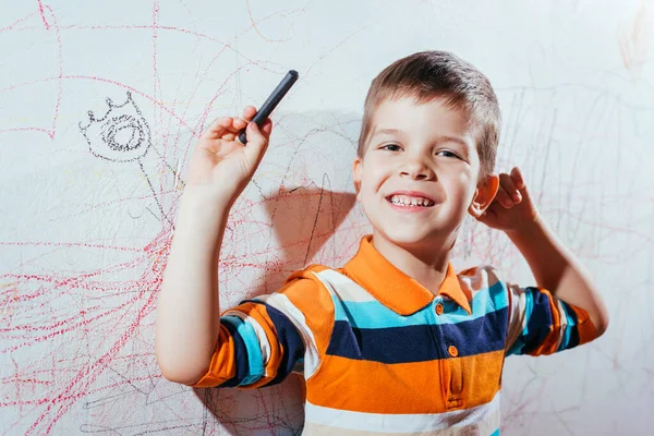 Laughing child draws on the wall with colored pencils