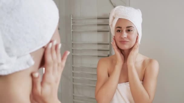 近距离观察，年轻女性头戴毛巾在脸上涂润肤霜，动作缓慢。光彩夺目的女性肌肤需要适当的营养。4k — 图库视频影像