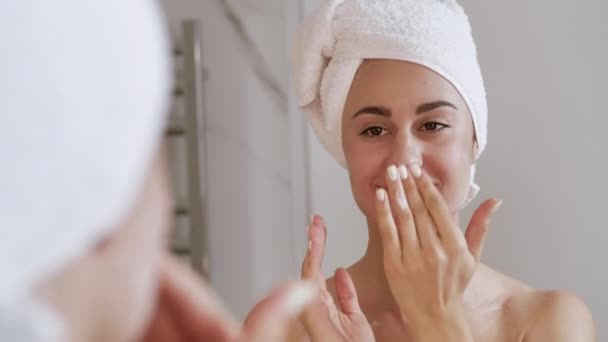 一名年轻女子在洗完澡后，在脸上涂上润肤霜，并用手指按摩。护肤自爱的概念。4k — 图库视频影像