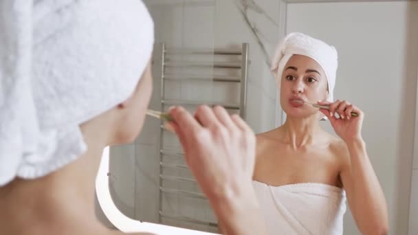 25 yaşında çekici bir kadın banyo aynasının yanında durmuş, dişlerini fırçalıyor. İşte benim 4K günümün başlangıcı. — Stok video
