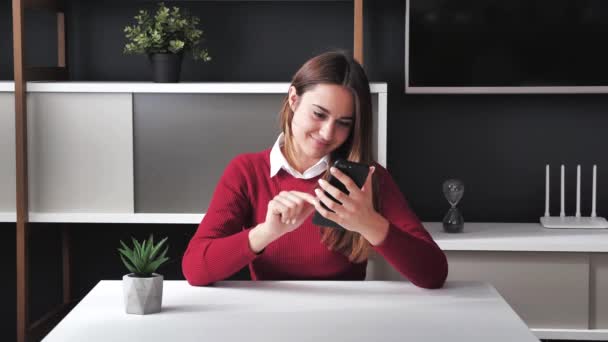 Sorrindo jovem mulher de negócios lendo notícias no telefone faz on-line uma compra sentar-se em casa mesa de escritório, feliz cliente do sexo feminino navegar na internet on-line site compras ordem entrega conceito 4k — Vídeo de Stock