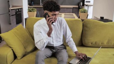 Modern daire 4k 'de rahat koltukta otururken genç afro afro portre iş adamı ya da öğrenci telefonla konuşuyor.
