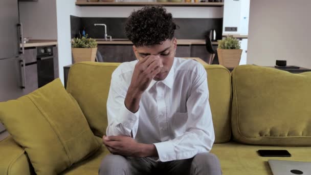 Cansado tipo de raza mixta sentado en el sofá siente dolor en sus ojos — Vídeos de Stock