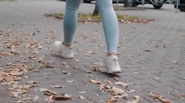 Sonbaharda kotlu sokak kızıyla yürür ve şirin spor ayakkabıları kaldırım taşlarına basar 4K