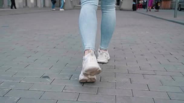 Promenades dans la rue fille en jeans légers et entraîneurs mignons marchent sur pavés urbain fond de ville ralenti 4k — Video