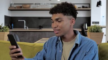 Teknoloji ve insanlar konsepti - gülümseyen Afro-Amerikan milenyumu akıllı telefonlu ev telefonlu 4K video görüşmesi.
