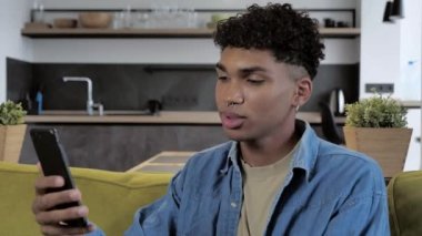 Teknoloji ve insanlar konsepti - gülümseyen Afro-Amerikan milenyumu akıllı telefonlu ev telefonlu 4K video görüşmesi.