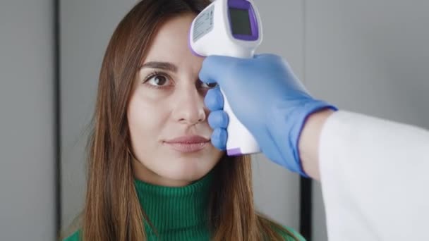 Close-up van een arts die een medisch gewaad inlevert met een contactloze infrarood thermometer over het voorhoofd van een jong meisje. Temperatuurcontrole concept. Ziektepreventie. Hoge temperatuur - niet — Stockvideo