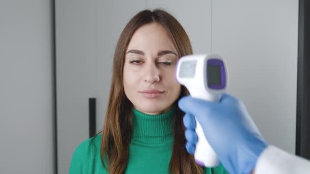 Primer plano de una mano de los médicos en una bata médica que sostiene un termómetro infrarrojo sin contacto sobre la frente de una niña. Concepto de control de temperatura. Prevención de enfermedades. Alta temperatura - No — Vídeo de stock