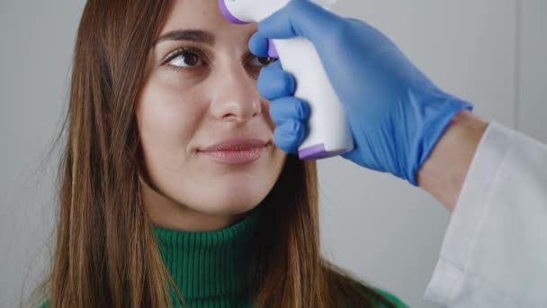 Männliche Ärzte reichen medizinische Handschuhe, die ein berührungsloses Infrarot-Thermometer über die Stirn einer Frau halten. Die Temperatur wird zu Hause gemessen. Epidemie. — Stockvideo