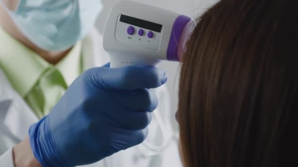 Инкогнизируемый врач-мужчина в защитной маске измеряет температуру пациентки с бесконтактным инфракрасным термометром. Обязательное измерение лихорадки. портативное устройство, необходимое во время — стоковое видео