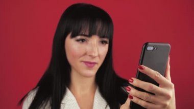 Mutlu bir kadın kırmızı arka planda cep telefonuyla heyecan verici bir şekilde haberlere bakıyor..