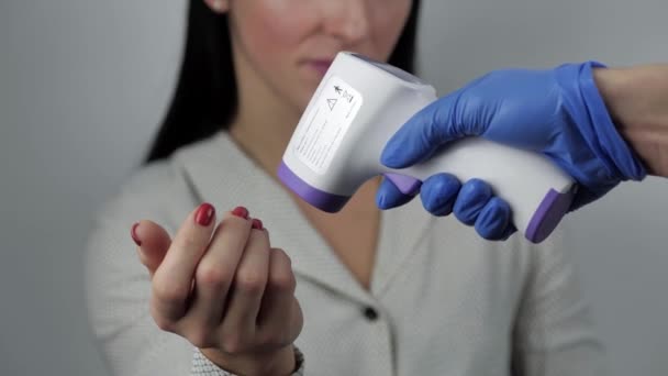 Een close-up. Artsen hand met handschoenen met contactloze digitale infrarood thermometer voor het screenen van vrouwelijke lichaamstemperatuur. — Stockvideo
