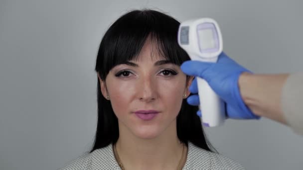 Großaufnahme einer Ärztin im Arztkittel, die einer 30-jährigen jungen Frau ein berührungsloses Infrarot-Thermometer über die Stirn hält. Temperatur-Check-Konzept. Prävention von Krankheiten. — Stockvideo