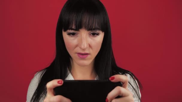 若い白人女性30年プロゲーマーは、赤の背景にスマートフォンでモバイルゲームをプレイゲームに勝つ. — ストック動画