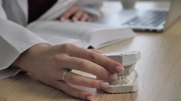 Ärztin Weibliche Hände halten ein 3D-Modell der Mundhöhle, Zahnbrücke. Lesen Sie Anatomie. Ausbildung Konzept Kieferorthopäde Ärzte Schreibtisch Hintergrund — Stockvideo