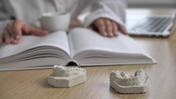 一个在模糊的背景下阅读解剖和喝咖啡的医生的工作台。专注于牙龈的石膏铸件 — 图库视频影像