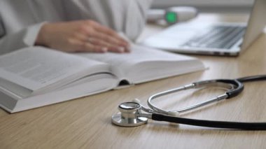 Tıp kitapları okuyan ve internette bulanık bir arka plan hakkında ek bilgi toplayan bir doktorun çalışma alanı. Steteskopa odaklan.