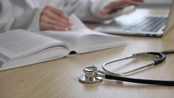 Stethoskop auf dem Klemmbrett und Arzt am Laptop auf dem Schreibtisch im Krankenhaus und Buch lesen, Gesundheitswesen und medizinisches Konzept, selektiver Fokus — Stockvideo