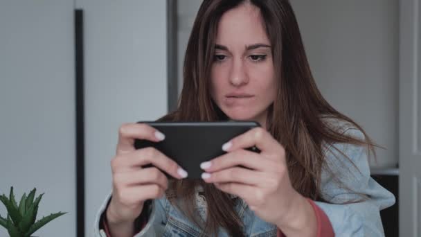 Közelkép egy fiatal nő farmerdzsekiben játszik az okostelefonján, átment a szinten, és boldogan kiabál igen — Stock videók