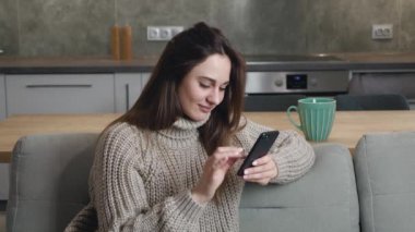 Bej renkli yün kazaklı güzel bir kadın kanepede oturuyor akıllı telefon mesajları atıyor, haberleri kontrol ediyor, sosyal medyada sörf yapıyor. Milenyum bayanı hücresiyle evde vakit geçiriyor.
