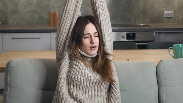 Medium schot van jonge vrouw stretching zijn armen en geeuw zitten in de bank in de keuken — Stockvideo