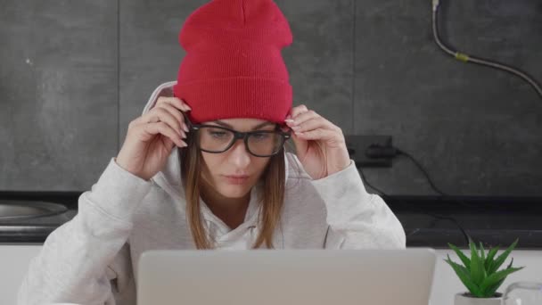 Удивительная молодая женщина шокирована, говоря "Вау". Красивая женщина в красном головном уборе удивлена, глядя на экран ноутбука на фоне интерьера. — стоковое видео