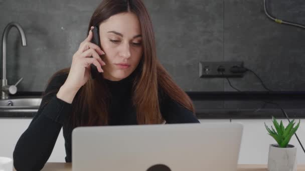 Serios young businesswoman professional talking on phone using laptop sit at the kitchen, female customer make mobile call confirming online website shopping order delivery concept — Stock Video