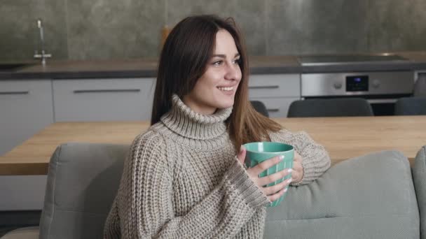 Молода жінка використовує смартфон, читаючи повідомлення соціальних мереж, насолоджуючись комфортним способом життя, п'ючи каву, що розслабляється на дивані вдома — стокове відео