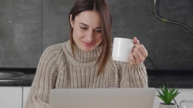 Yünlü süveter giyen bin yıllık genç bayan bilgisayarda yazışıyor evde kahve içiyor ve tek başına eğleniyor.