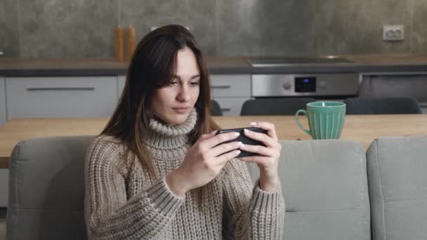 Hazard młoda kobieta kaukaska dziewczyna 20 lat w wełnianym swetrze, pozowanie za pomocą telefonu komórkowego odtwarzania trzymać gadżet smartfon wideo gry PC izolowane na nowoczesnym tle wnętrza. Szczęście kocha — Wideo stockowe