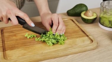 Ahşap tahtada marul doğrayan kadın elleri. Evde yemek yiyorum. Yiyecek endüstrisi. Genç bayan mutfak masasında yemek hazırlıyor..