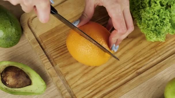 Kvinnor skalar apelsin. Skivad apelsin och avokado på bordet. Föda, få kalorier, vegetarianism, naturliga vitaminer. — Stockvideo