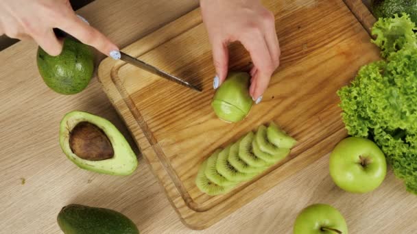 Vrouwen snijden verse groene kiwi 's. Bovenaanzicht. Keuken achtergrond. — Stockvideo