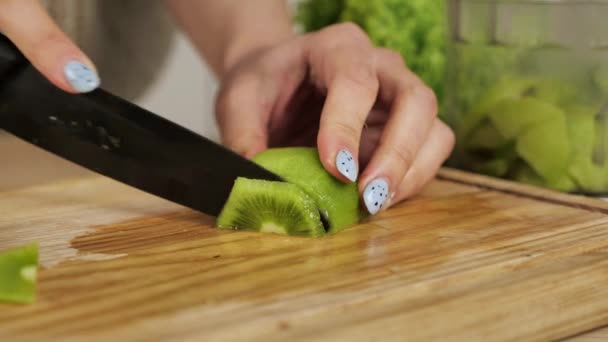 Rebanando kiwi en trozos pequeños, con un cuchillo de cerámica, en una tabla de cortar de bambú — Vídeo de stock