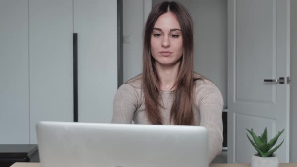 Молодая, скучающая деловая женщина с ноутбуком сидит за столом дома и делает массаж головы в современном офисном доме — стоковое видео