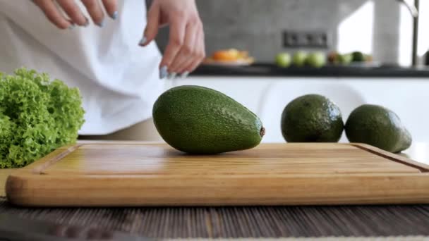 Las manos femeninas muestran un aguacate cortado en 2 partes. Comida vegana. Interior de cocina — Vídeos de Stock