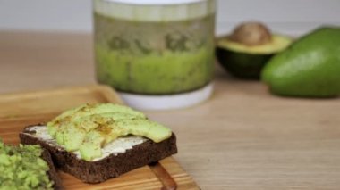 Tahta arka planda avokado ve guacomole parçaları ile tost. Sağlıklı beslenme konsepti, bitkisel ilaçlar. Arka planda yeşil taze smoothie