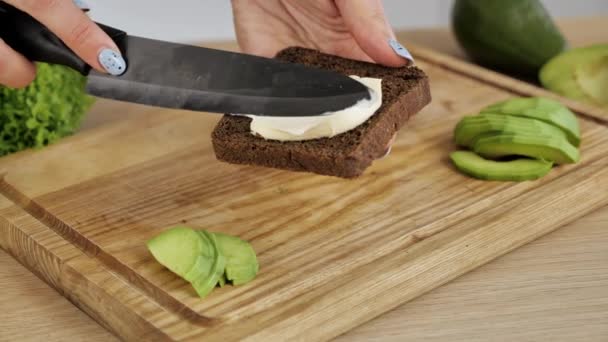 Mano femminile che fa pane tostato di avocado sano su tavola di legno. Sesamo e semi di lino. Cibo vegetariano — Video Stock